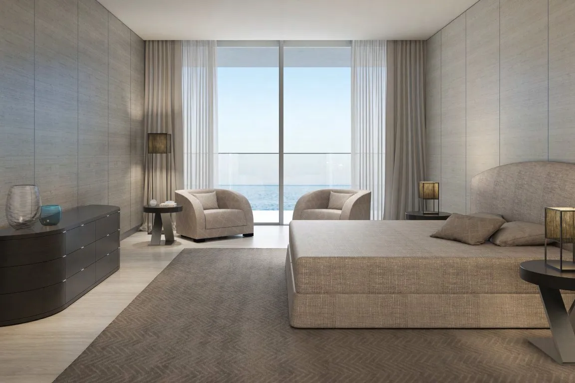 Bedroom with upholstered bed, armchairs and full-height window onto the sea